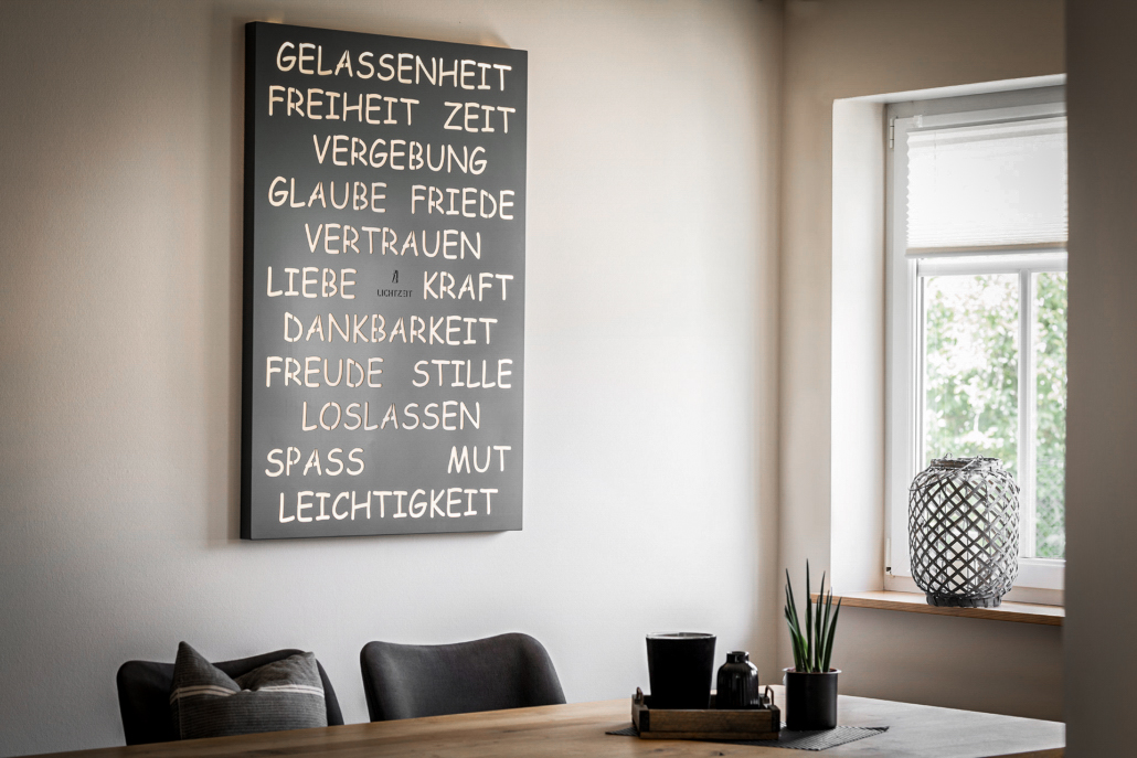 Hängendes Kraft-Licht-Werk mit verschiedenen Wörtern an der Wand und davorstehendem Tisch